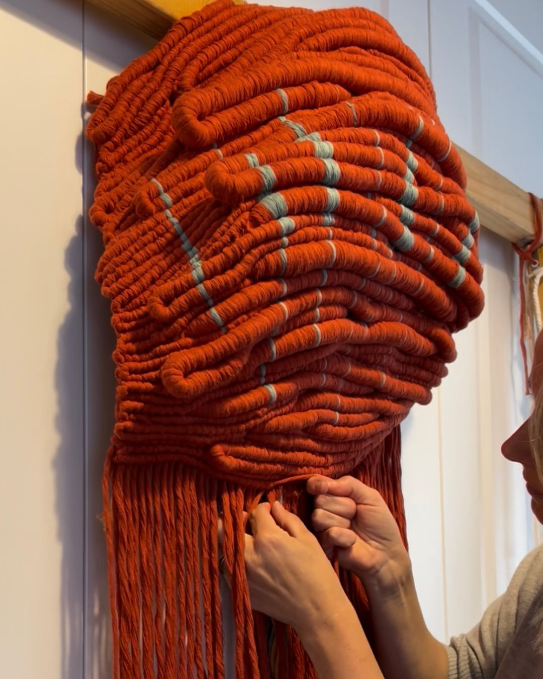 Kasia Dudkiewicz hand-knotting Wounded Healer, showing the slow making process behind the red sculptural textile artwork.
