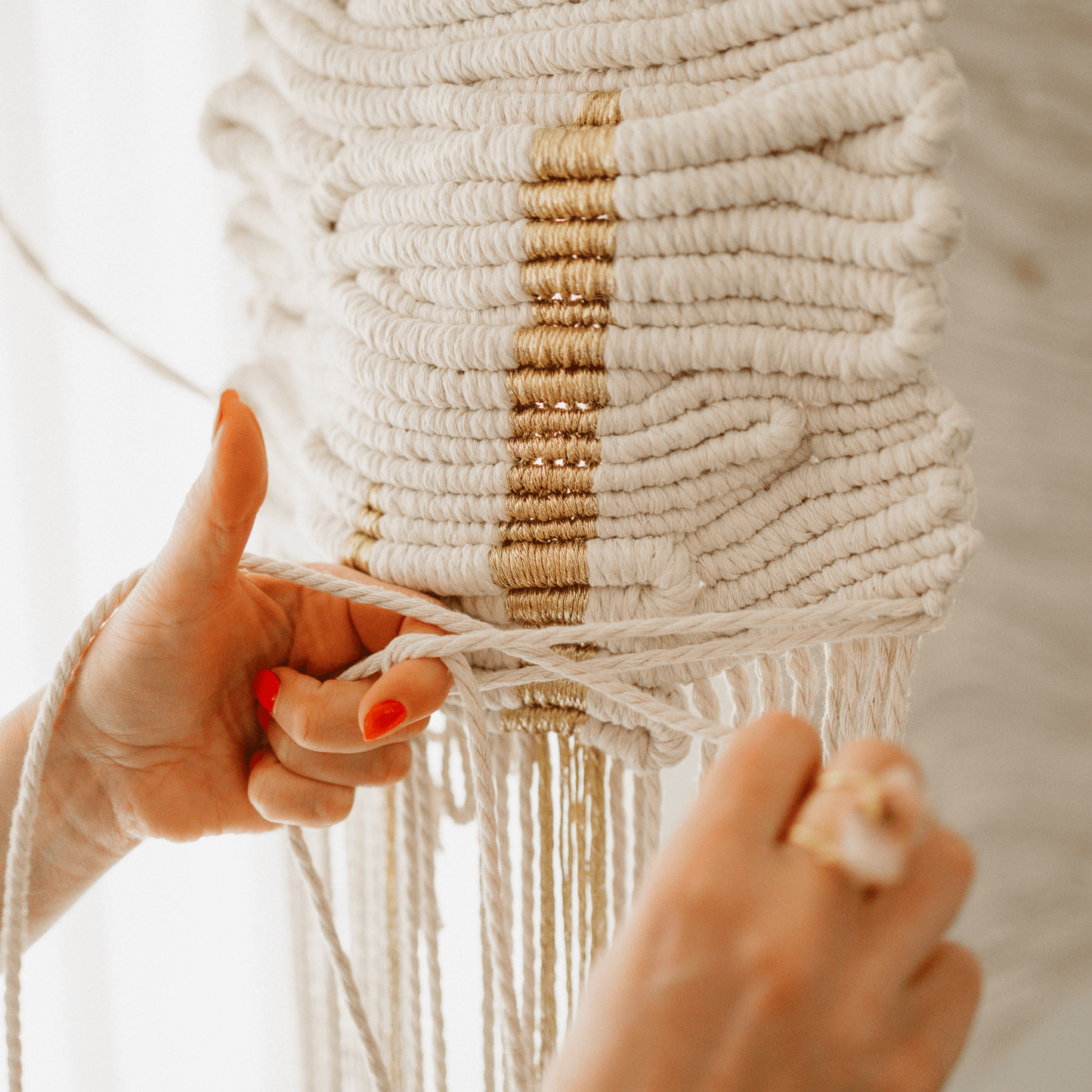 Close-up of a hand holding a sculptural wall hanging with white and gold threads.