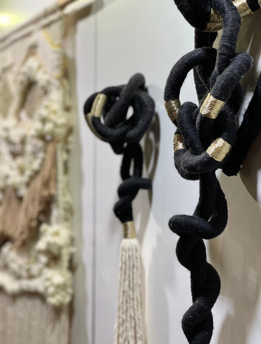 Close-up of a custom fibre art installation featuring black twisted ropes with gold accents, contrasted by white and neutral woven textures in the background.