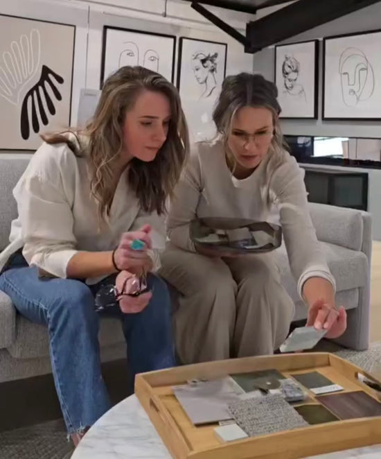 Two women in a room with art on the wall, looking at color swatches, knotted by hand