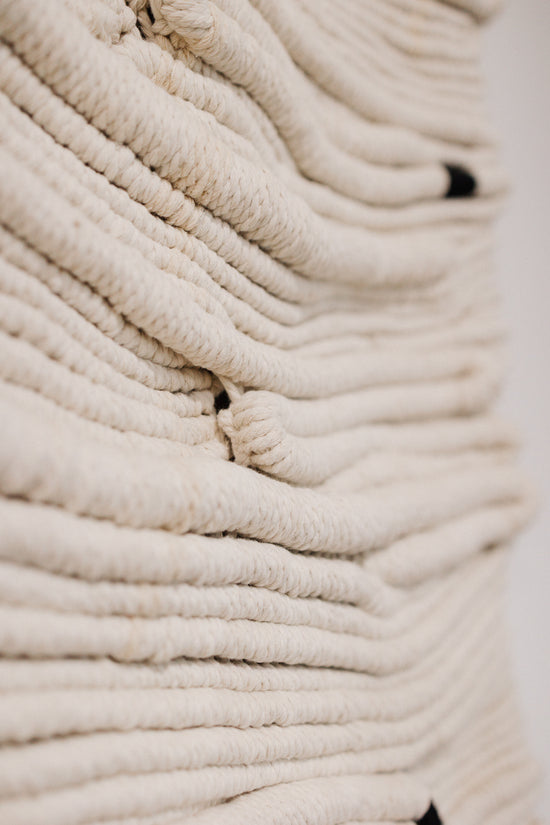 Close-up of a textured beige fibre art with a blurred background, knotted by hand