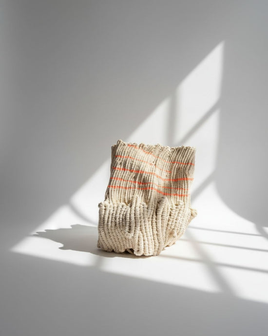 Textured handwoven sculpture with striped pattern on a white surface with shadows, knotted by hand