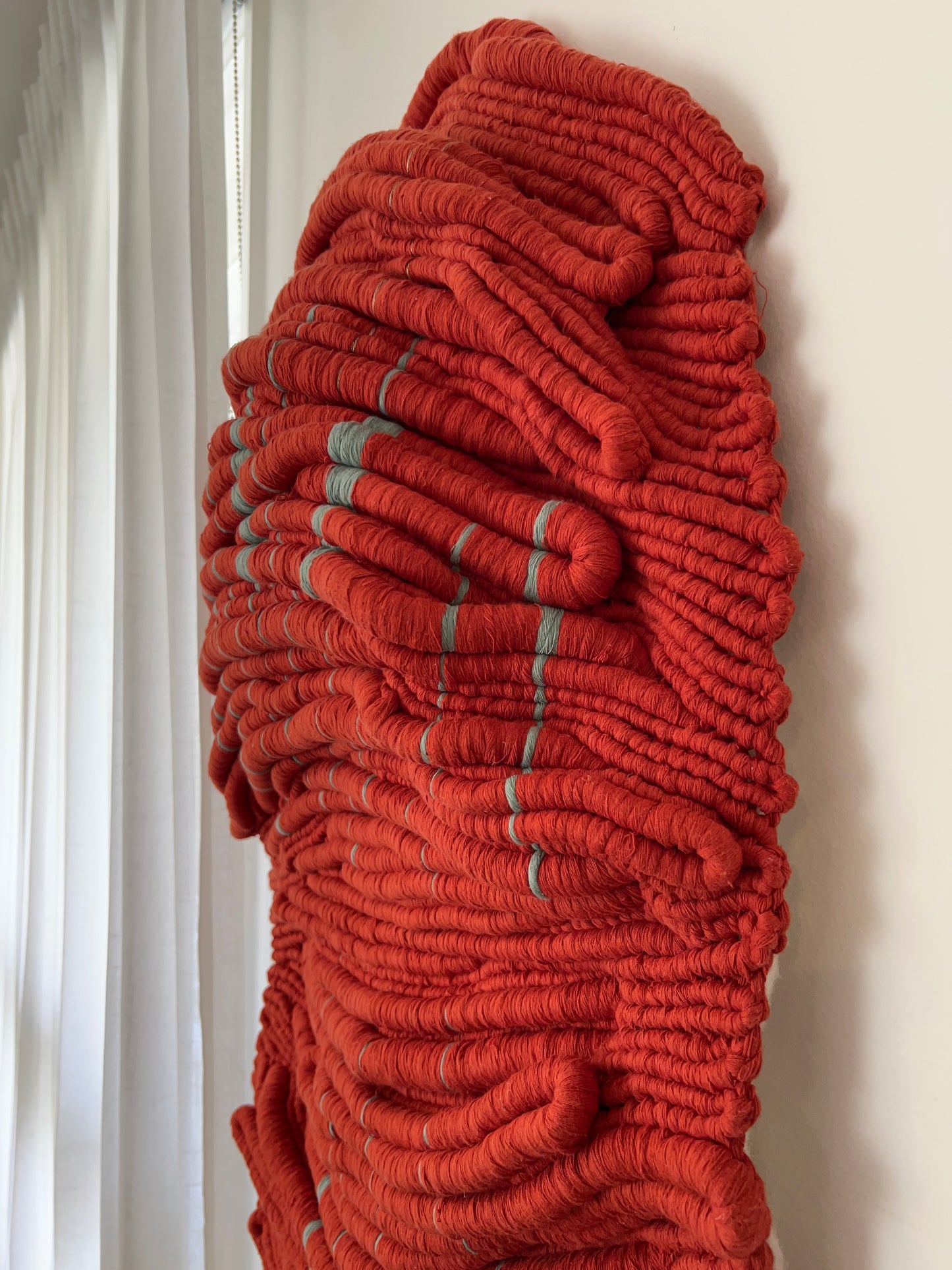 Close-up of Wounded Healer showing the layered hand-knotted red fibres, pale blue details and sculptural textile relief.