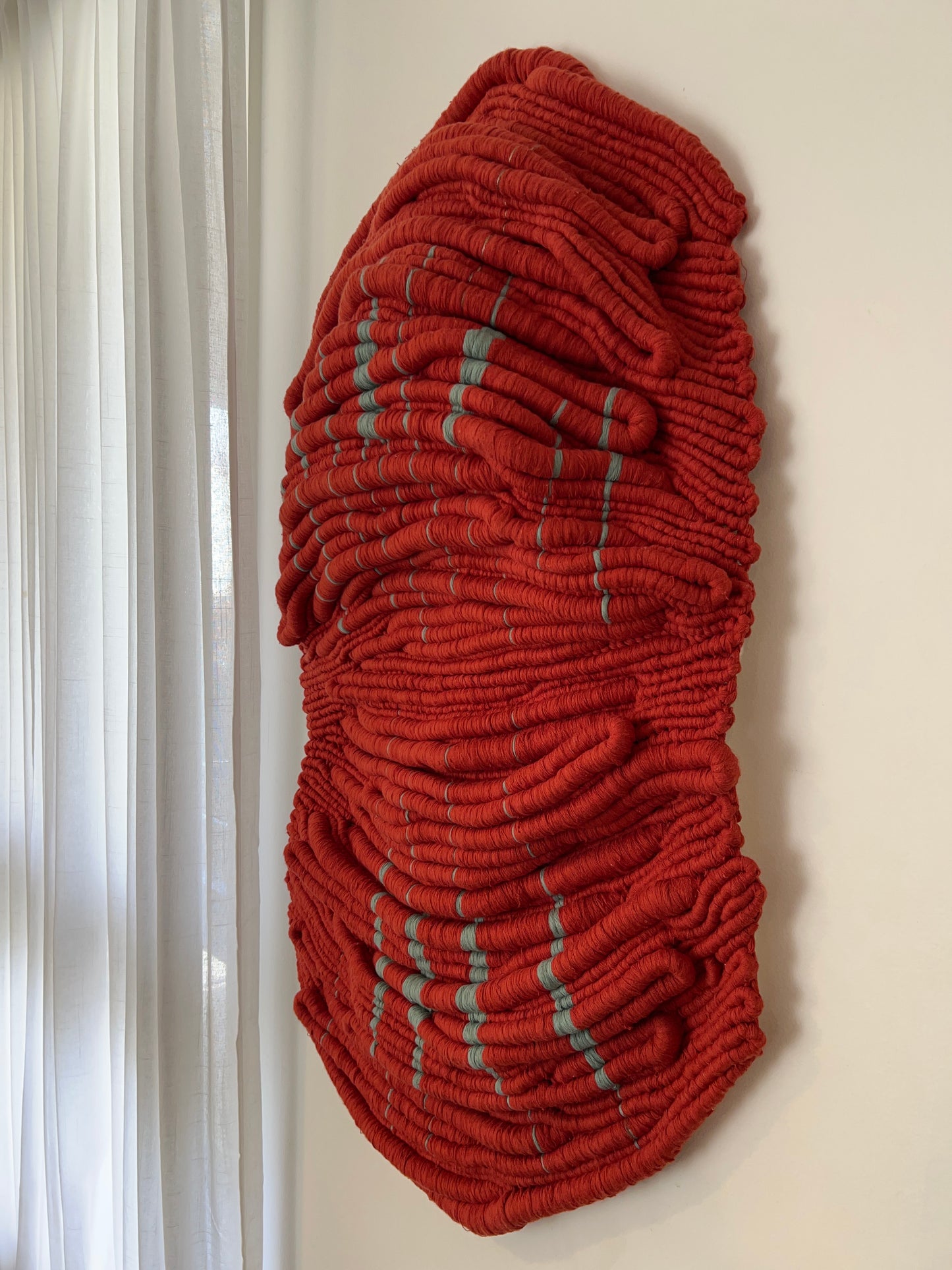 Angled view of Wounded Healer, a red hand-knotted sculptural textile artwork with pale green details by Kasia Dudkiewicz.